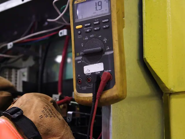 Mãos de eletricista com luvas num quadro de fios, com o multímetro ao lado
